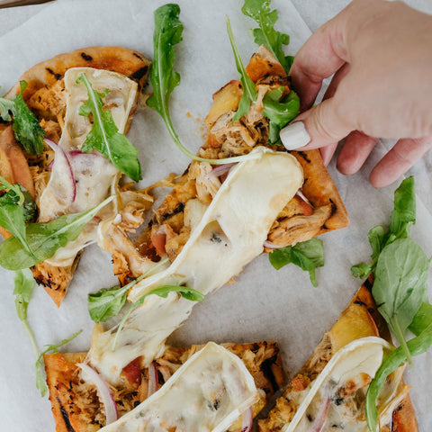 Hand picking up a slice of flatbread with cheese and greens on a marble surface