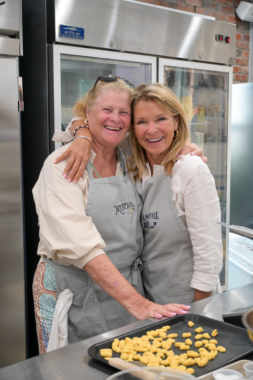 Two guests in Mercantile aprons smiling beside a tray of handmade pasta