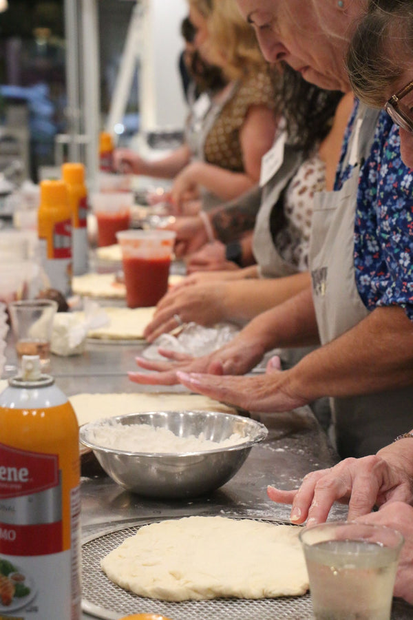 A row of guests shaping pizza dough at the kitchen counter